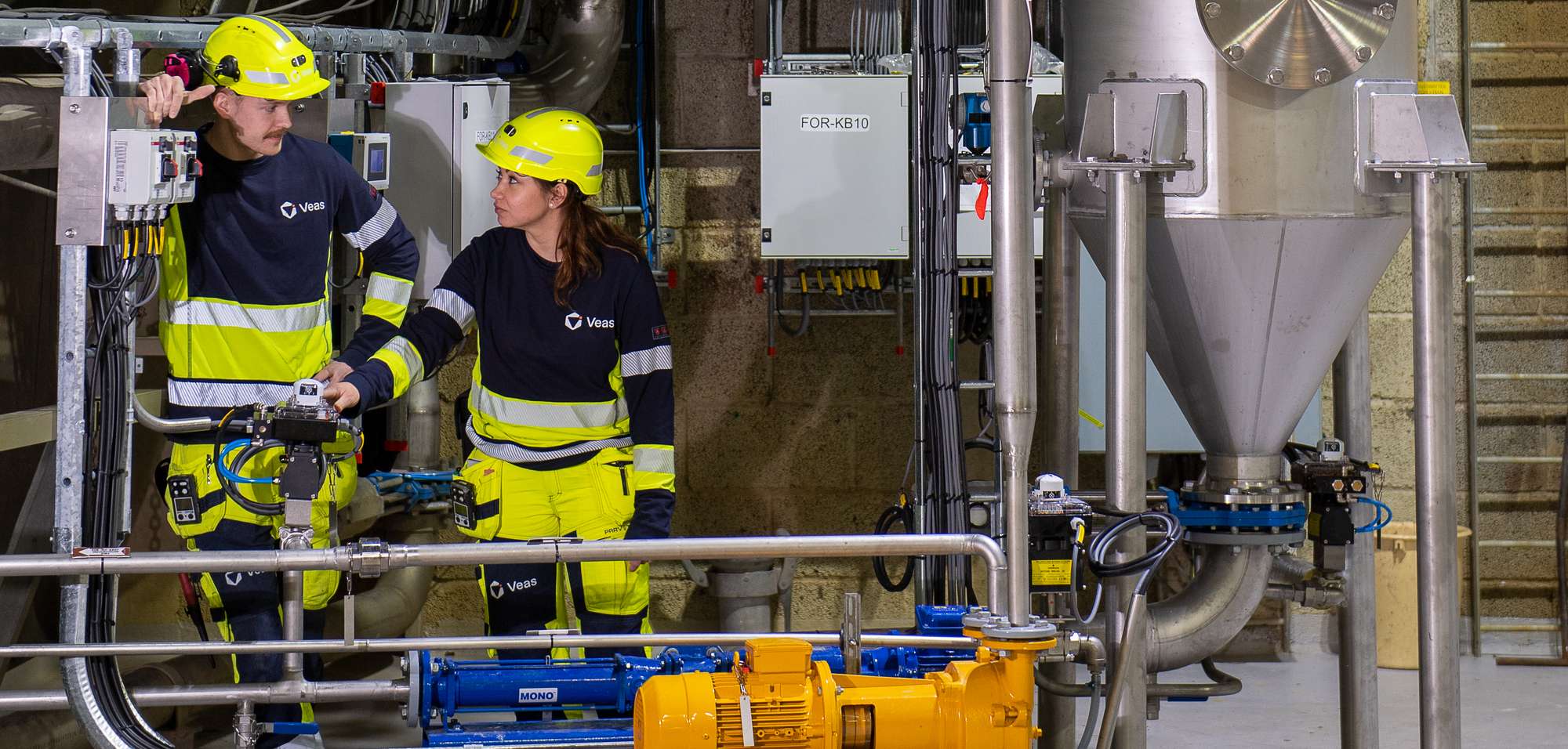 En kvinnelig og en mannlig arbeider i sorte og gule arbeidsklær inkludert en gul hjelm